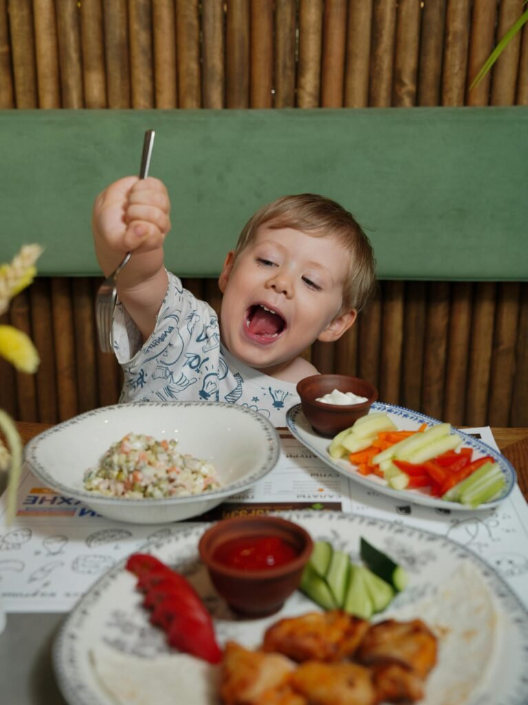 A cheerful child eagerly eating a healthy meal with vegetables and dip, creating a joyful moment.