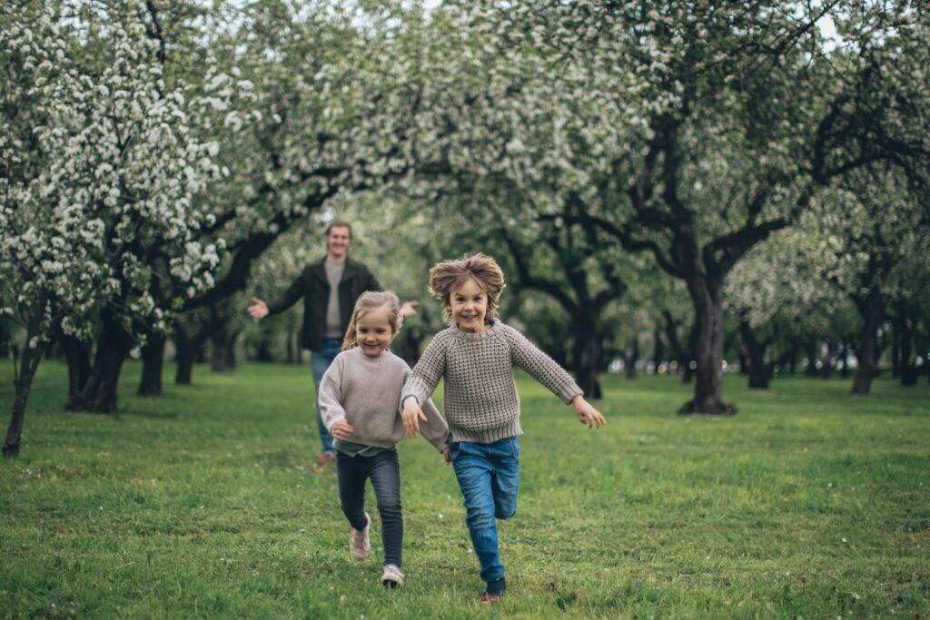A cheerful father and two children running through a blossoming park, enjoying springtime together.